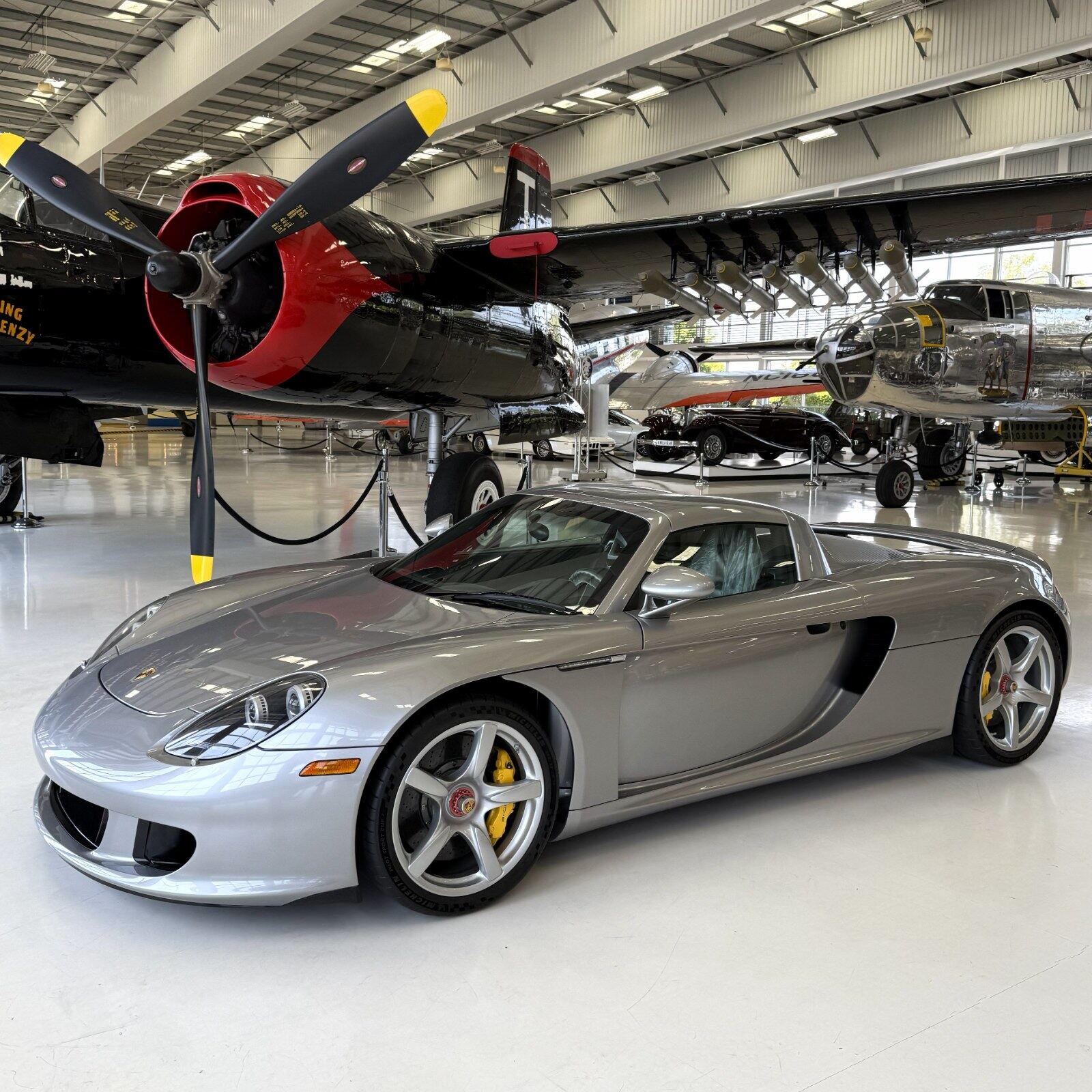 A silver Porsche Carrera GT among vintage warbirds in a private hangar